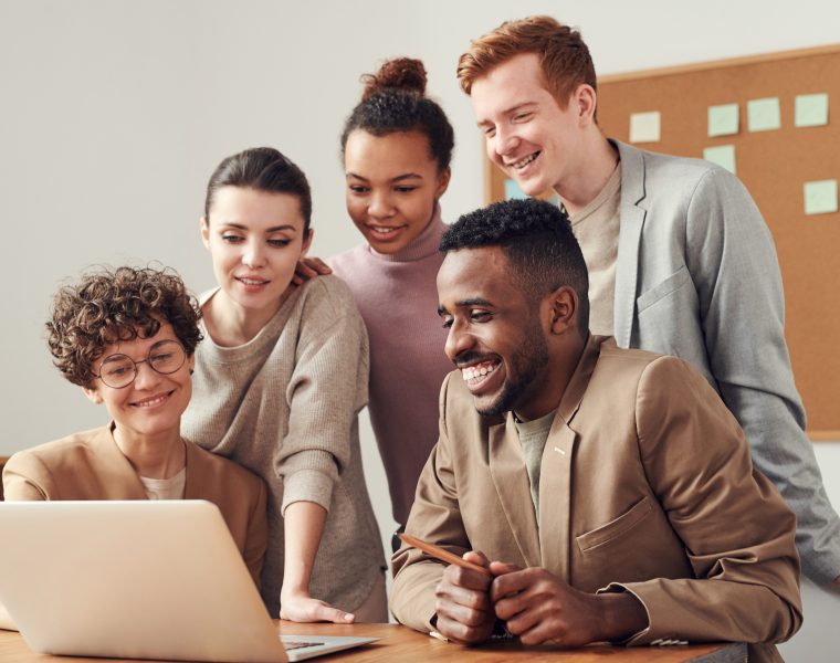 Diverse group of People standing at a table commenting on what they see on a laptop.